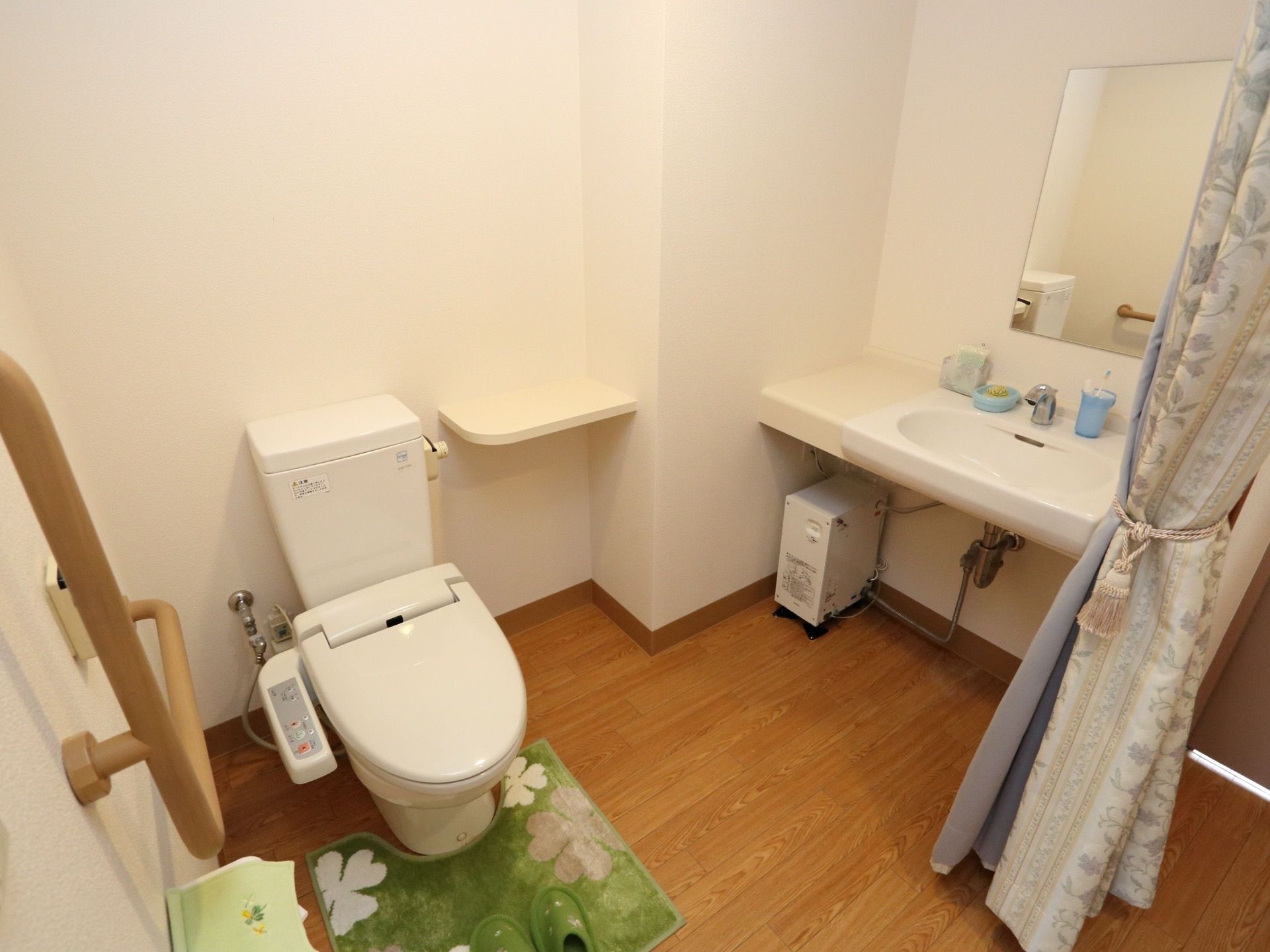 温水洗浄機能付きのトイレは、広いスペースになっている。右側には洗面台があり、水色のコップやトレーが置いてある。