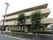 玄関の前方から、建物全体を写したものである。道路沿いには大きな木が植えてあり、左端には電柱が設置されている。