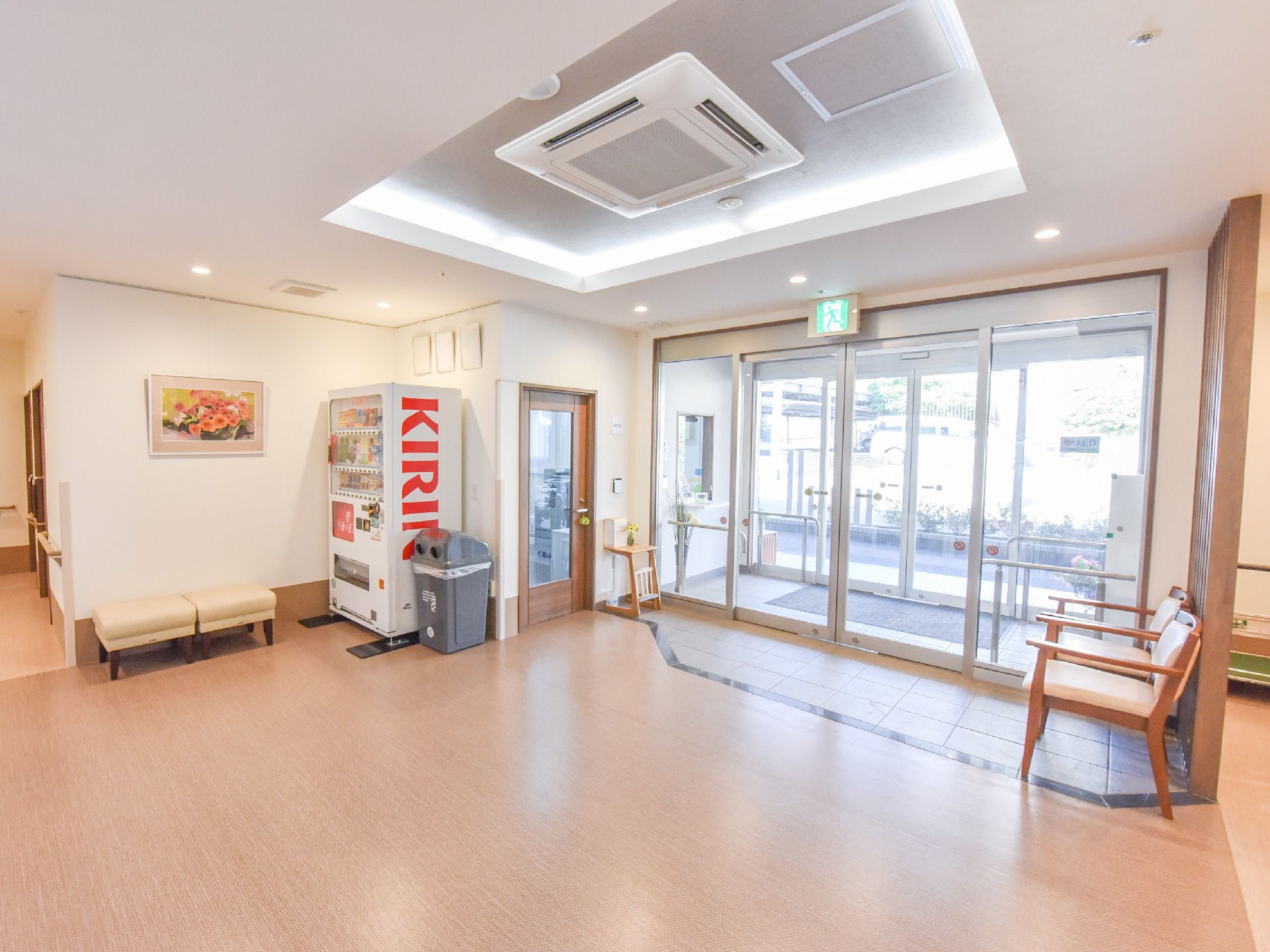 玄関から入ってきて右側に椅子が二つ並べられている。左側には自動販売機も設置してある。壁には手すりあり。