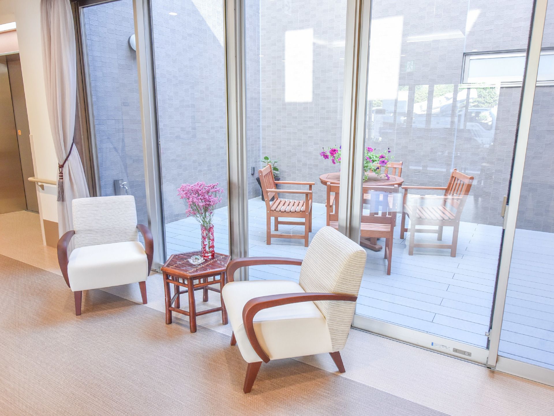 部屋からはテラスが見えテーブルとイスが置かれている。机には花が飾られている。窓が大きくとても開放的である。