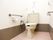 トイレの両側の壁に手すりが付いている。右の手すりの上にナースコールが設置してある。床はピンク色で、壁の下3分の1ほどが茶色で塗られている。