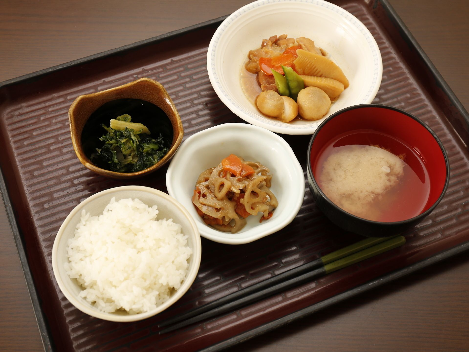 茶色の角盆の上に、ご飯と汁物、小鉢、大小の椀が乗っている。小鉢には青物野菜が入っており、大きな椀には里芋とタケノコの煮物が盛り付けてある。
