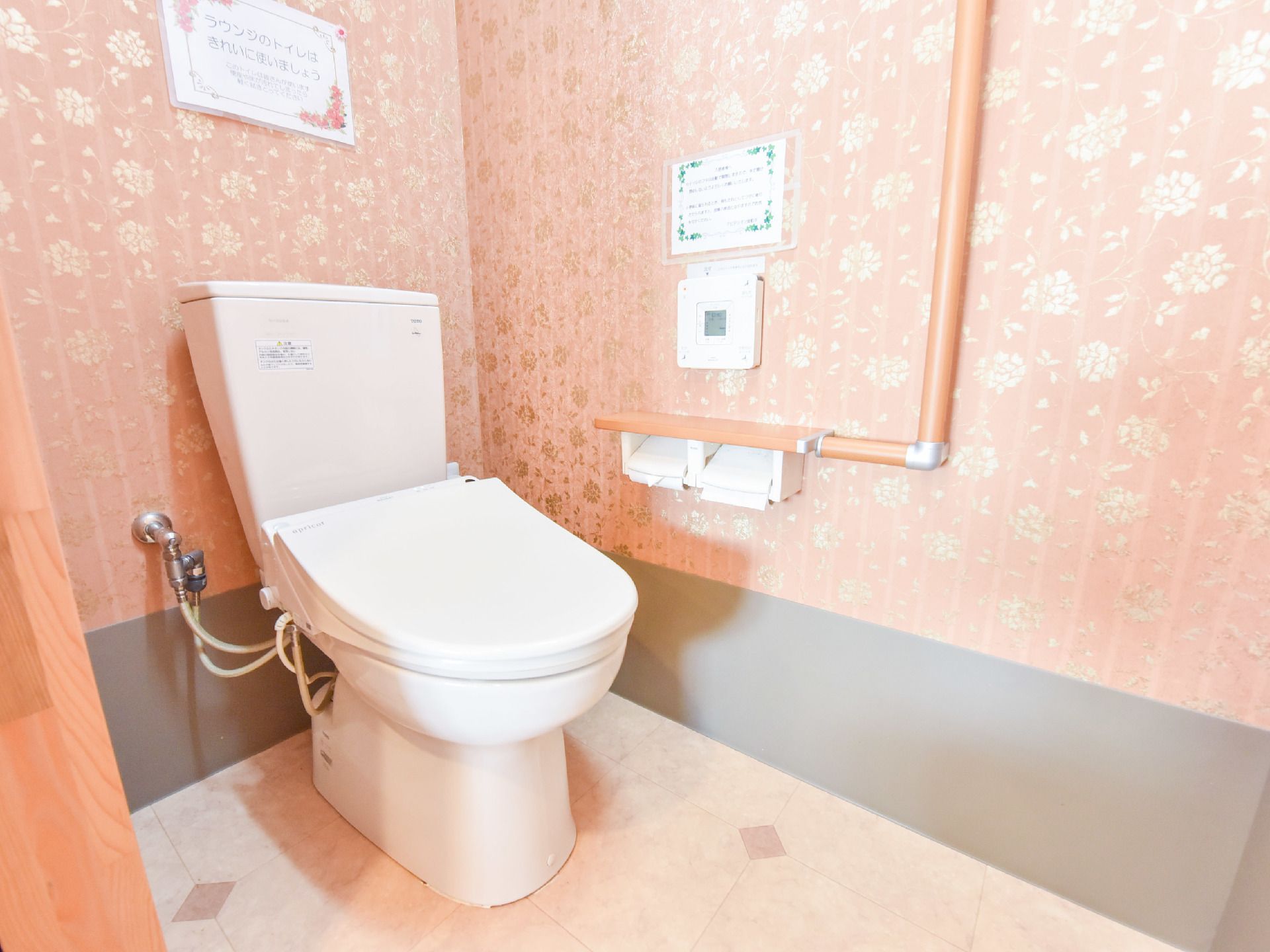 トイレの内装はラウンジと共通。トイレは水洗トイレ。壁にはL字型の手すりとペーパー、トイレのスイッチが設置されている。壁には貼り紙。