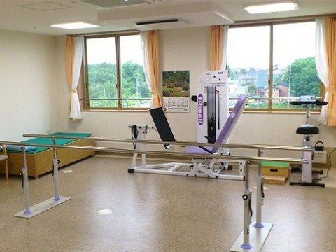 中央部に歩行訓練器、窓際に自転車漕ぎマシンが置かれているリハビリ室