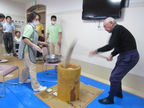 杵でお餅をついている男性入居者様と、水をつけている女性スタッフ