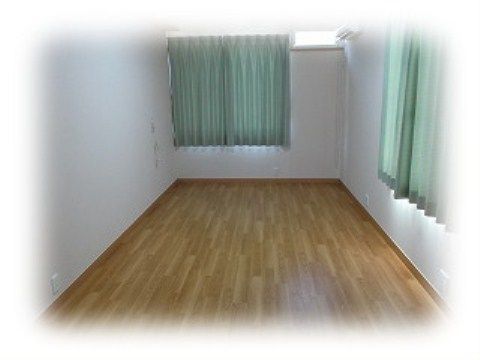 緑色のカーテンが取り付けられたワンルームの居室。ナチュラルブラウンの木目調のフローリングの床となっている。