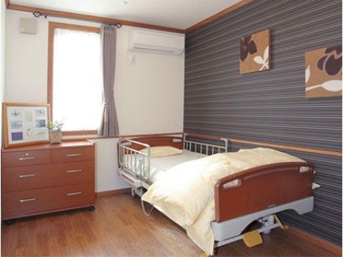 介護ベッドが置かれている。窓の横にはエアコンが付いている。ベッド側の壁は白ではなくストライプ模様になっている。