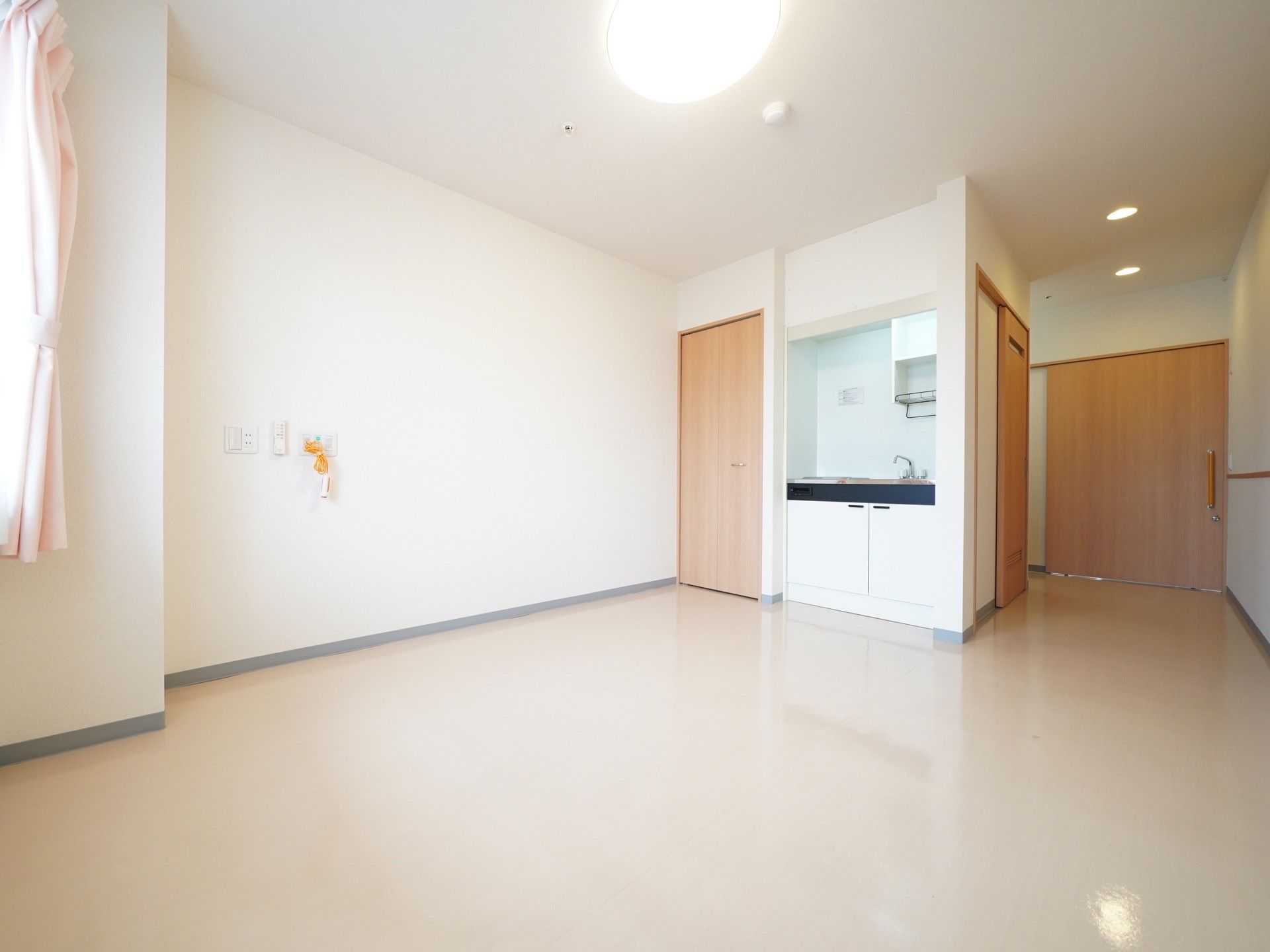 居室は広々としており、窓には薄いピンク色のカーテンがかけられている。コンパクトなキッチンも完備されている。