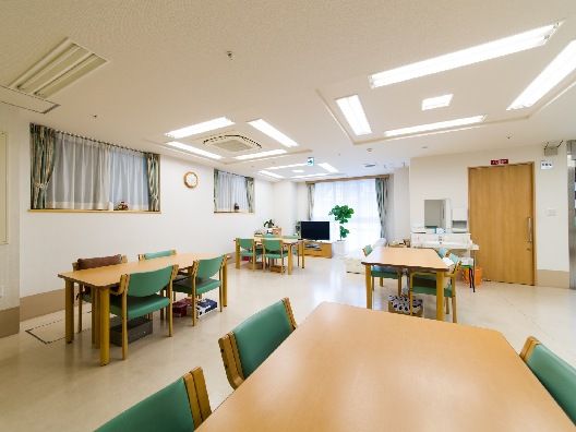 緑の椅子がセットされたダイニングテーブルセットが複数あり、観葉植物や時計が飾られている。