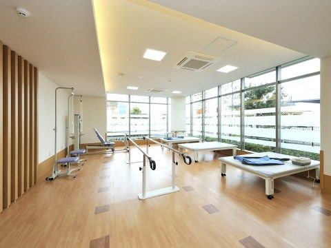 窓が大きくとられ、室内の明るさは十分である。床は木目調で、歩行訓練用の平行棒やプラットフォームなどのリハビリ機器が置かれている。