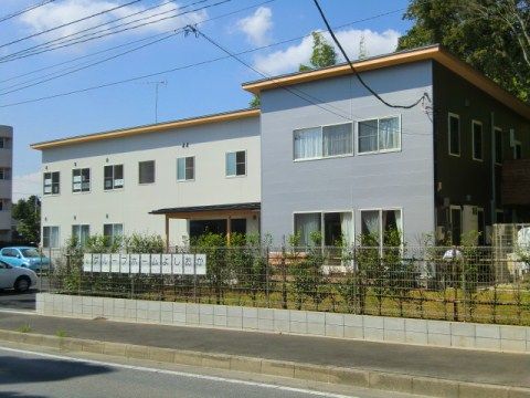 歩道沿いのフェンスの内側に生け垣が設けられている施設外観