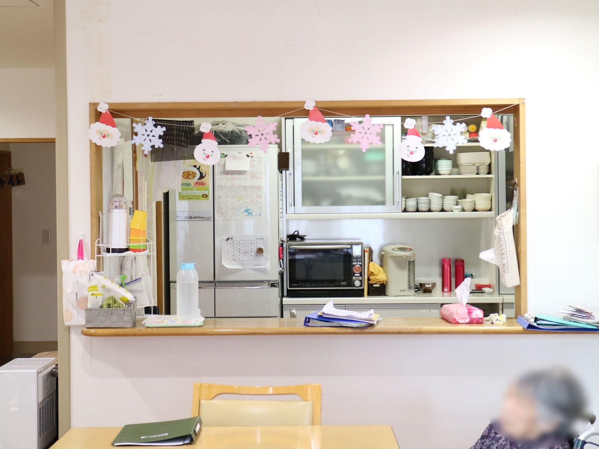 キッチン内に冷蔵庫や食器棚、電子レンジやポットが置かれている。カウンターの上部には、クリスマスの飾りつけが施されている。