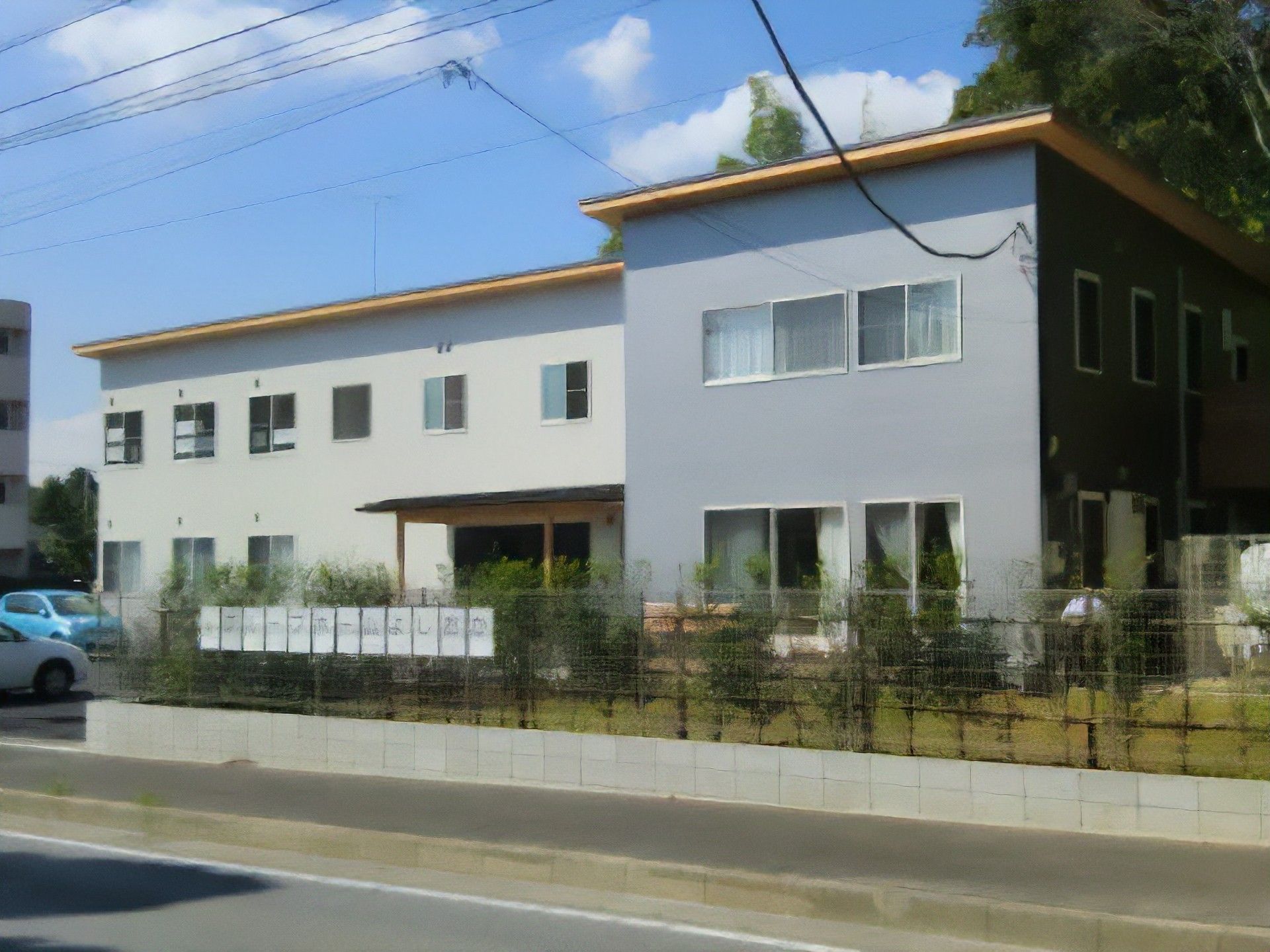 歩道沿いのフェンスの内側に生け垣が設けられている施設外観