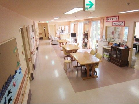 フローリングの広いスペースがある。床はピンク色で通路がベージュ色になっている。左側の壁には手作りの作品が飾られている。