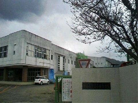 支援学校の校門付近の様子。入口には白い壁があり、施設名が表示されている。奥に白色の建物があり、１階部分は吹き抜けになっている。