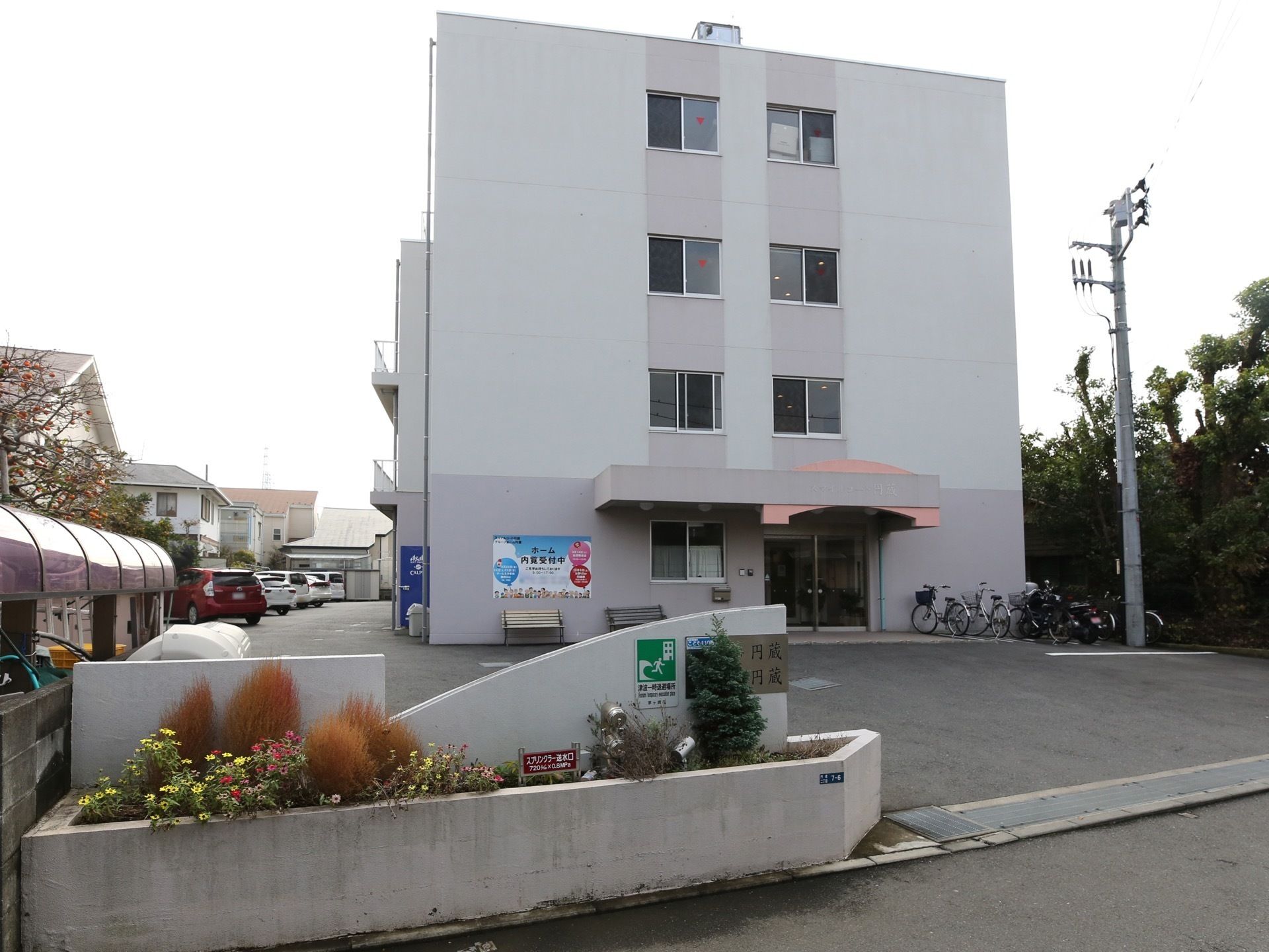 アスファルトで舗装された敷地に３階建ての住宅が建っている。建物の横には駐車場と駐輪スペースが設けられている。