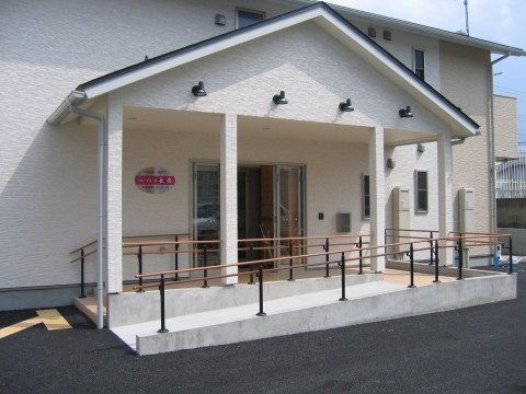 折れ曲がった緩やかなスロープが設置されている、三角屋根のひさしがついた玄関
