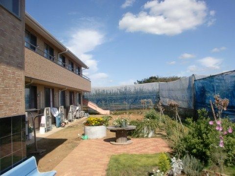 2階建ての茶色い建物と、花壇やベンチのある、視界の開けた庭