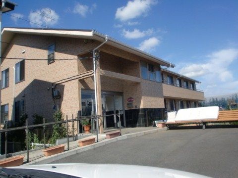 上り坂の上にある茶色い建物と、玄関に設けられたプランターや木のベンチ