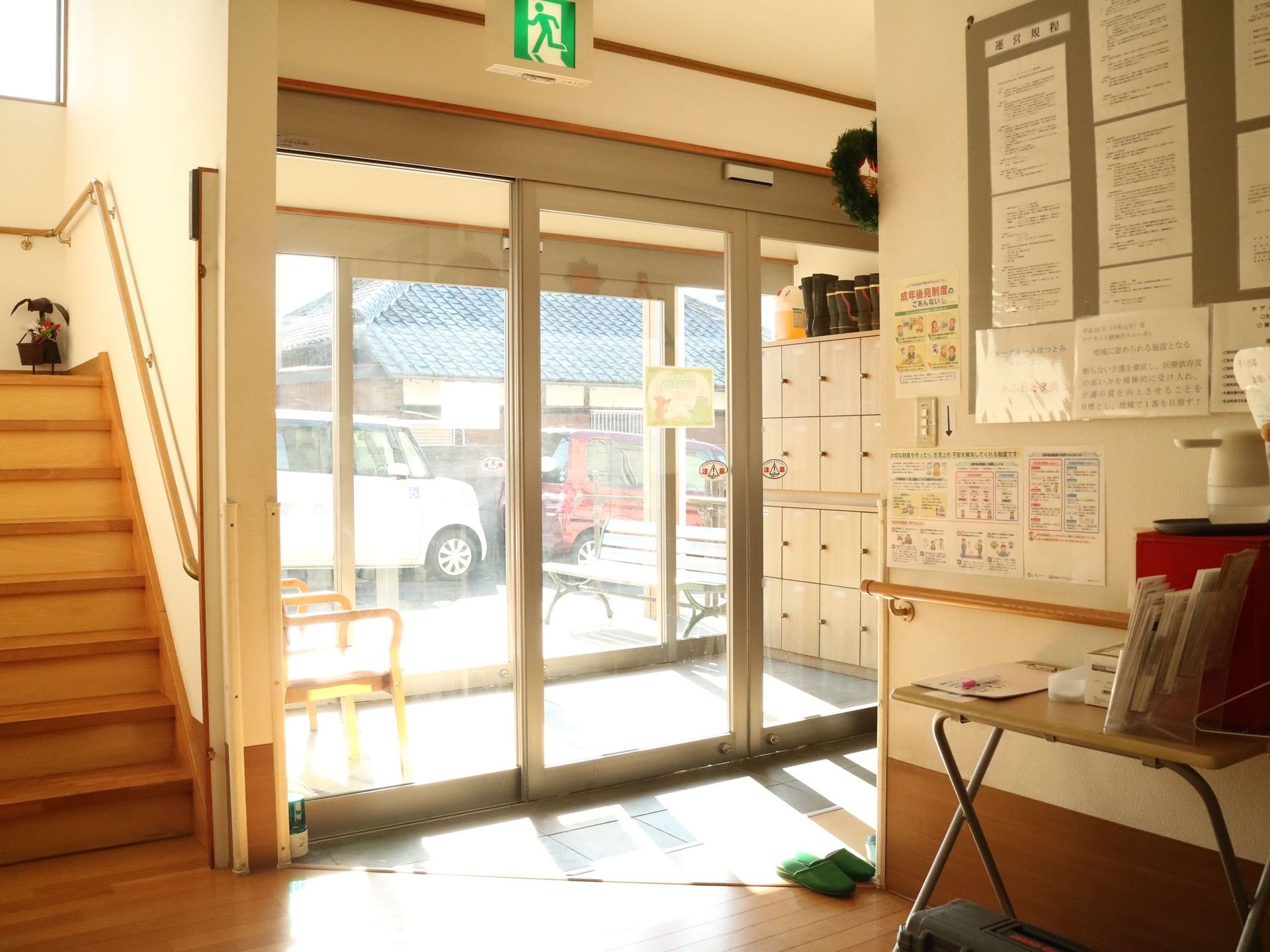 ガラス窓の嵌められた自動扉の入口が中央にある。入口左手には上階へ上がる階段がある。右手の壁には紙がたくさん貼られている。