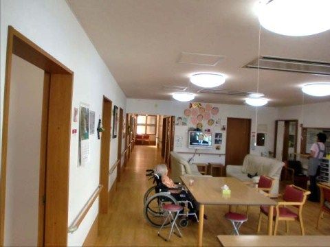 個室の入り口が並ぶ廊下と、車椅子でテーブルにつく入居者が見える食堂