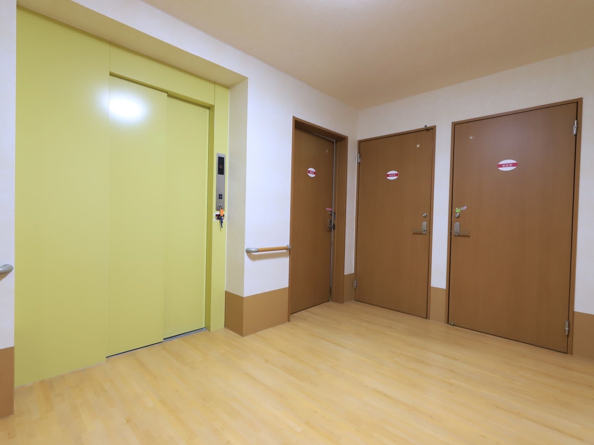 黄色く塗られたエレベーターのすぐ手前まで手すりが伸びており、ボタンを押して待機する間も体を支えられる。