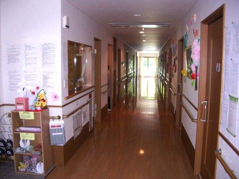 清潔感のある明るいバリアフリー仕様の廊下である。壁には入居者様の作品や連絡事項が一面に掲示されている。