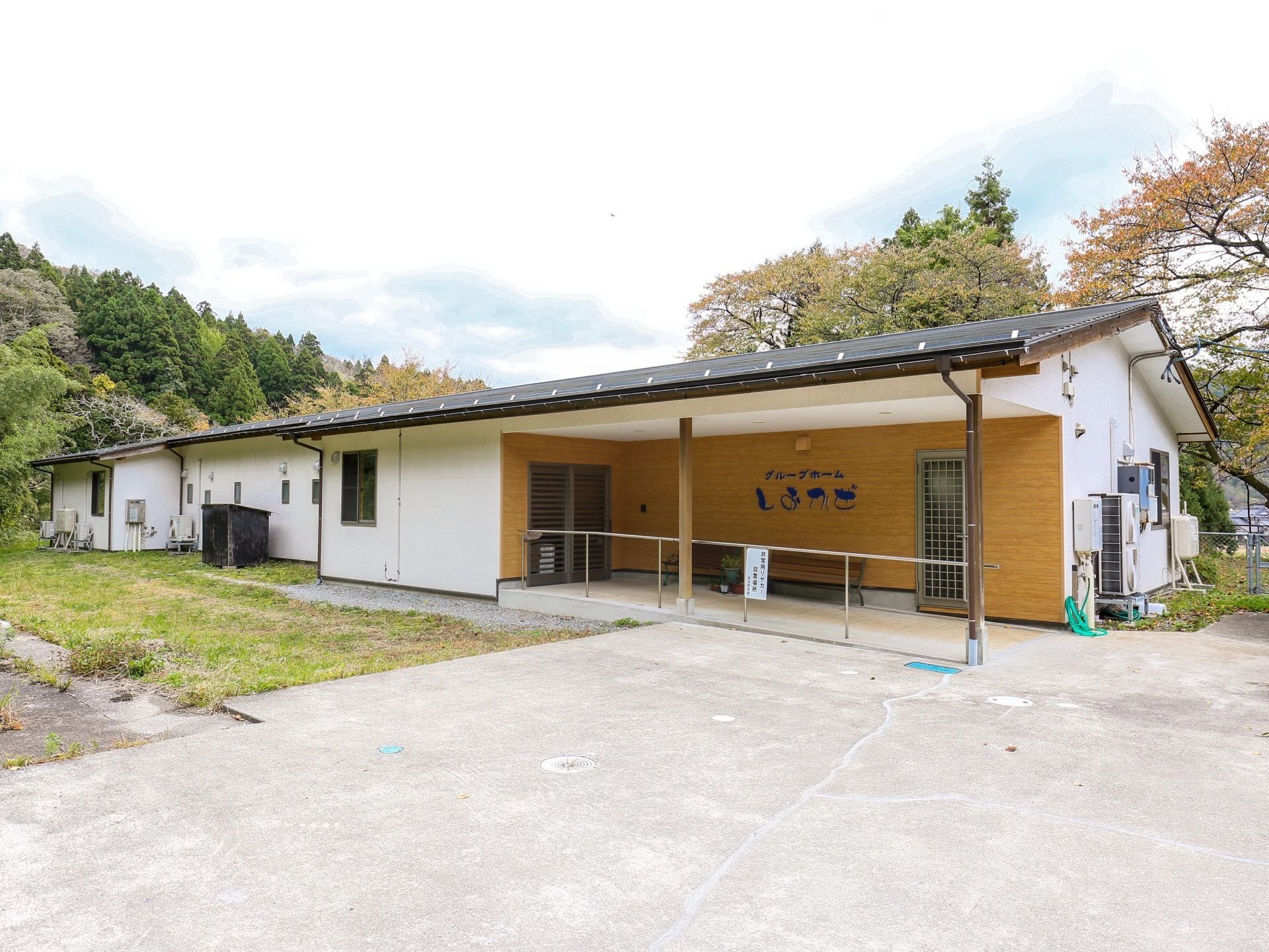 玄関側から施設を見た図である。白い壁に黒い三角の屋根が乗った建物である。中央に玄関があり、スロープがある。