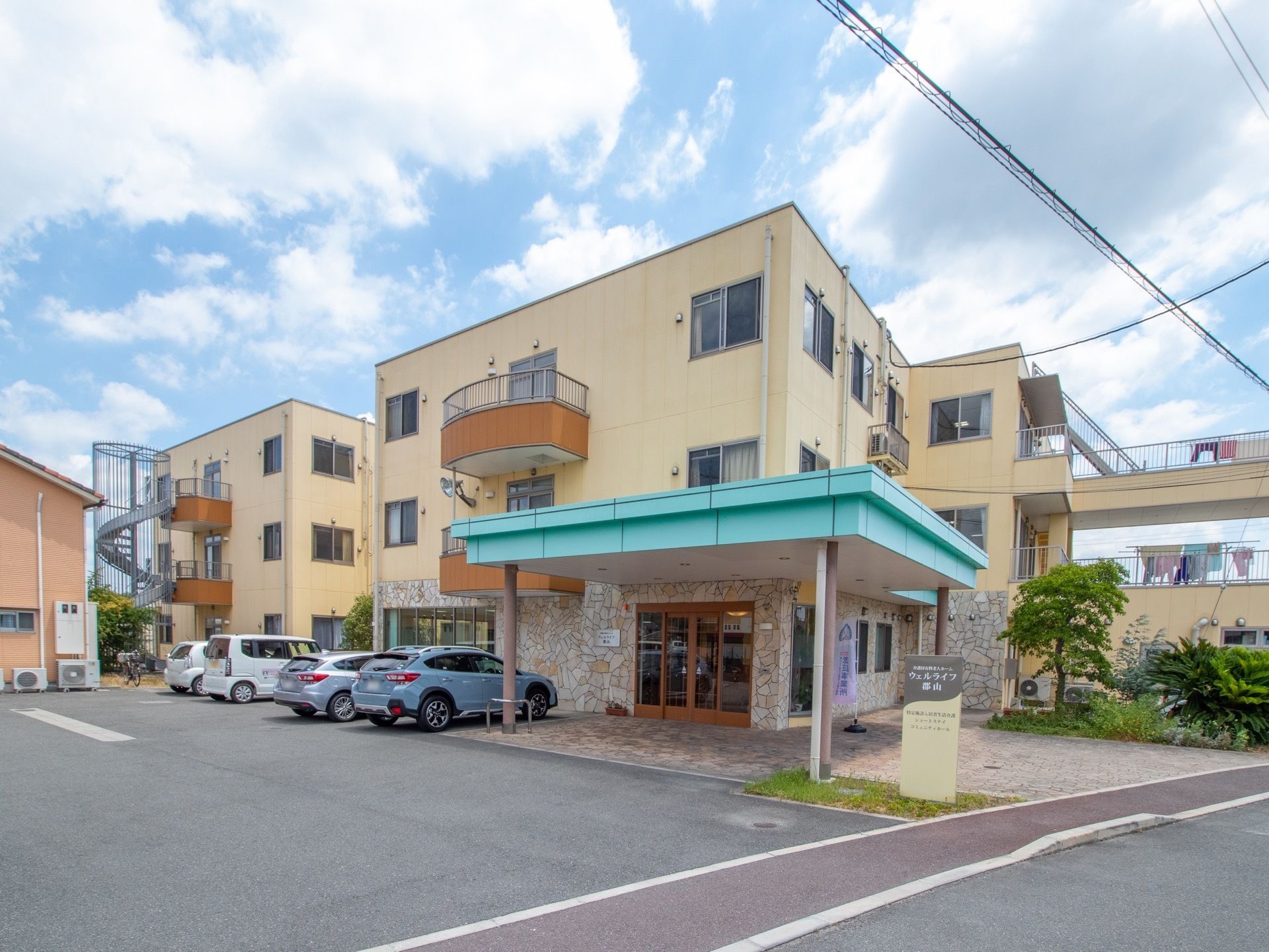 施設の外観は色合いが綺麗で上品な印象である。建物の前に駐車スペースがある。入り口は自動ドアで段差がないので入りやすくなっている。