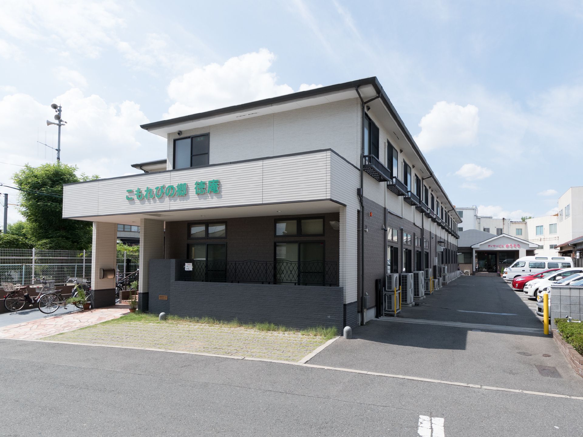 奥行きのあるライトグレーの2階建ての建物とそれに沿った駐車場