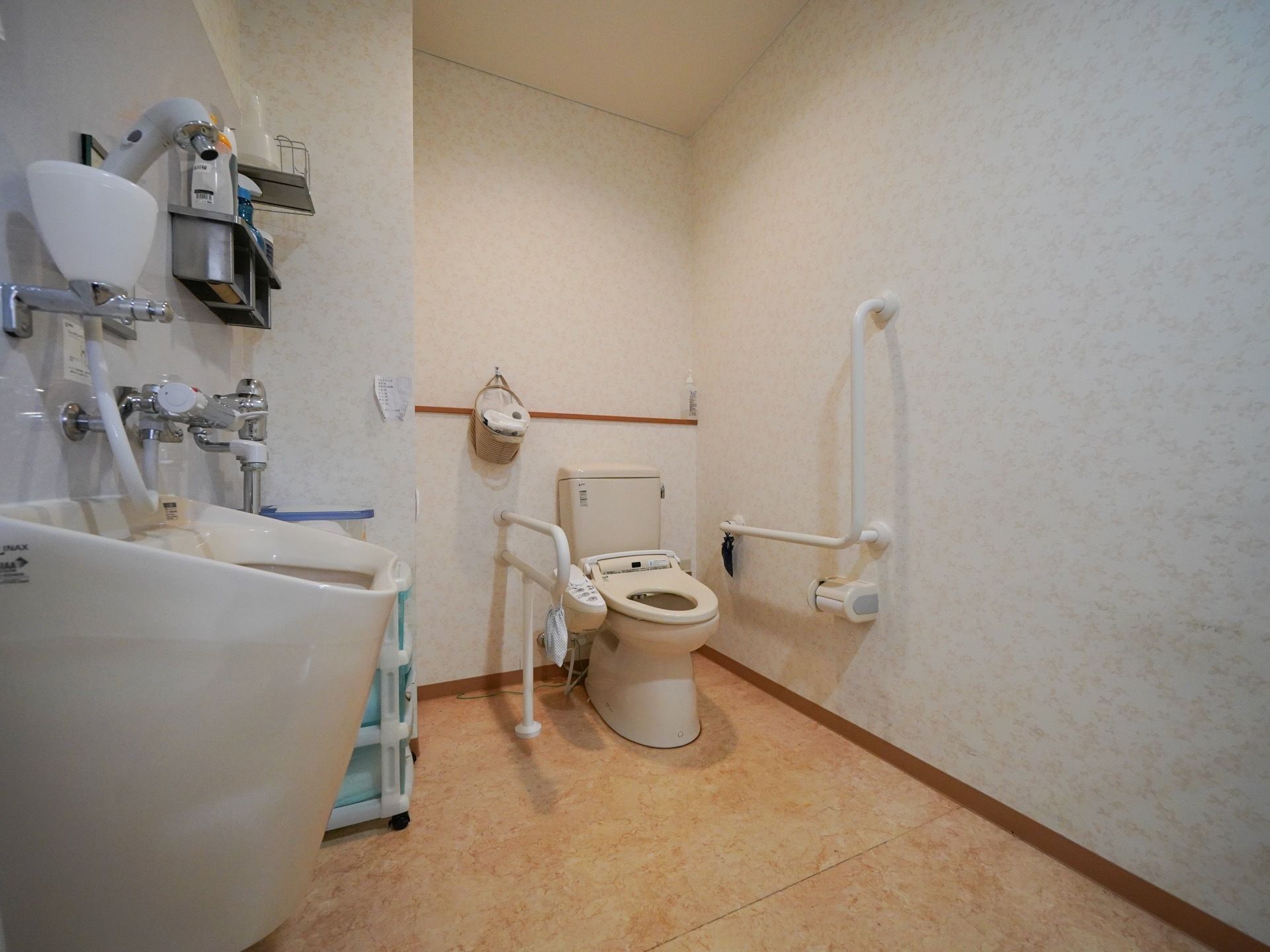 開放感のある、広々したトイレである。温水洗浄便座が完備されており、左右に白色の手すりも設置されている。