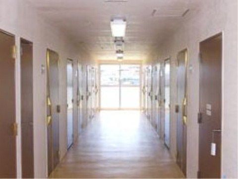 広く長い通路の奥は窓になっていて、光が差し込んでいる。通路の両側に各居室の扉が設置され、天井に照明が取り付けられている。