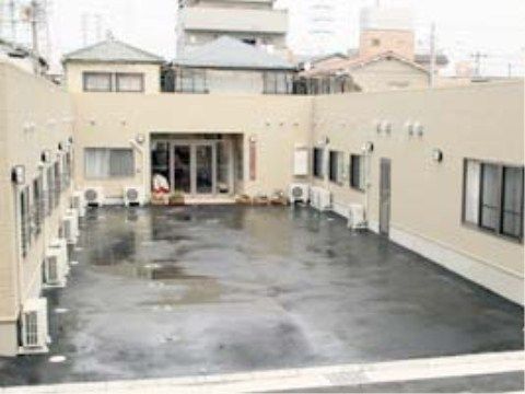 駐車場があり、それをコの字に囲むように建っている薄い色の建物