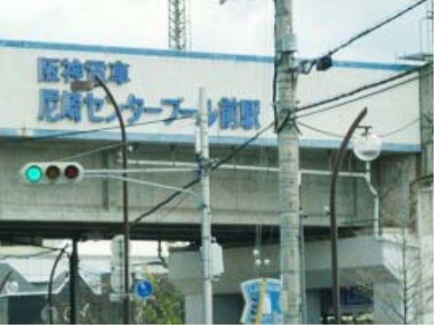 施設の最寄り駅である。高架にある駅で、壁面に青い文字で駅名が書かれている。駅の下にコンビニがあり、大きな道路が通っている。