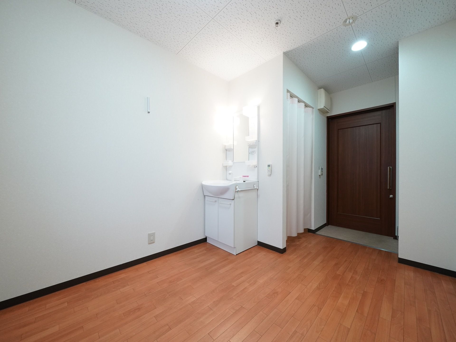 ダークブラウンの大きな引き戸の入り口で、入ってすぐにトイレが備わっている。トイレは扉の代わりにカーテンがついている。