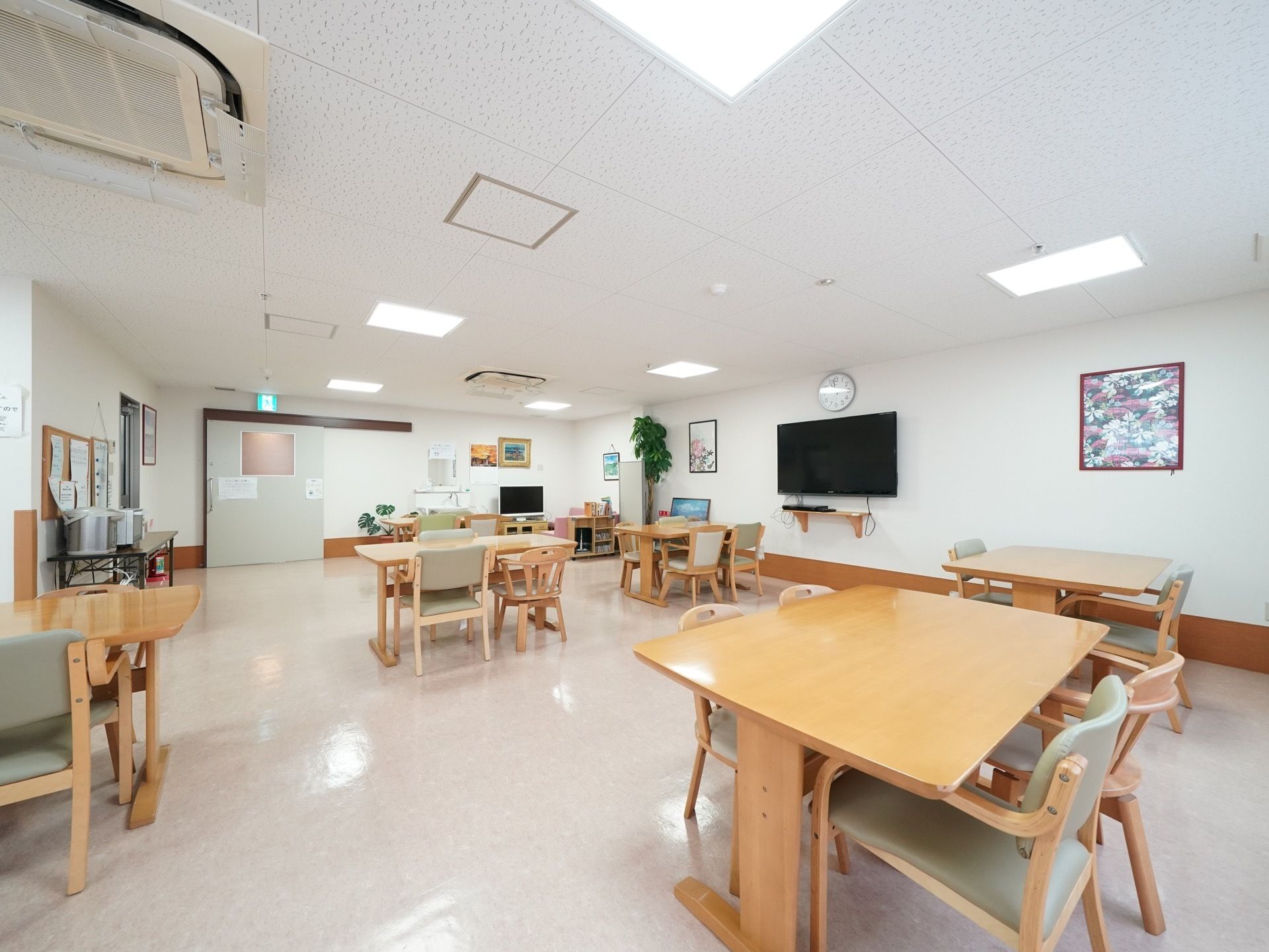 クッションフロアの広々とした食堂に、間隔をあけてダイニングテーブルが並んでいる。テレビが複数設置されている。