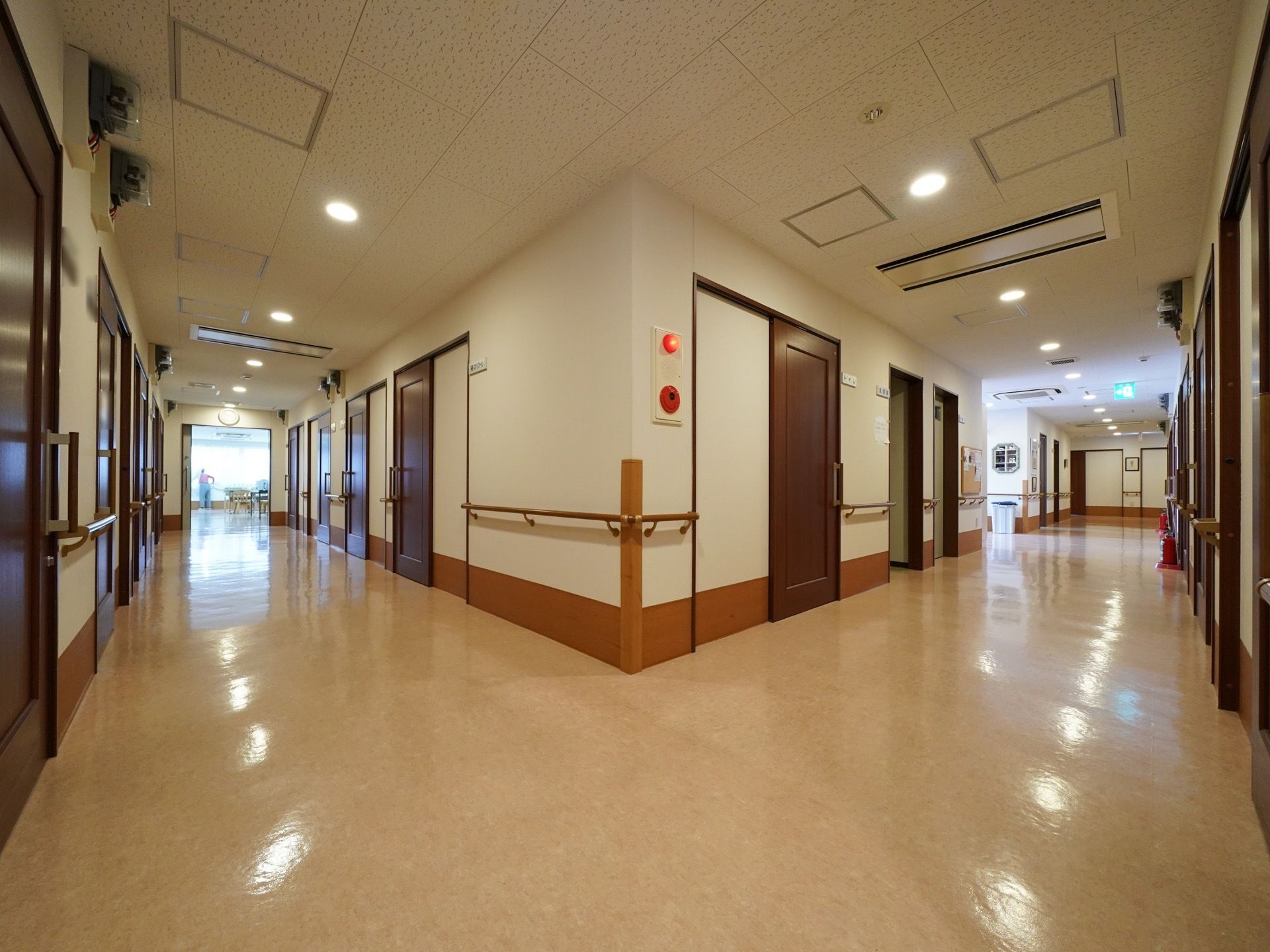 廊下の両側の壁に、手すりと居室のドアが並んでいる。ドアはダークブラウンのスライドドアである。左の突き当たりに食堂がある。