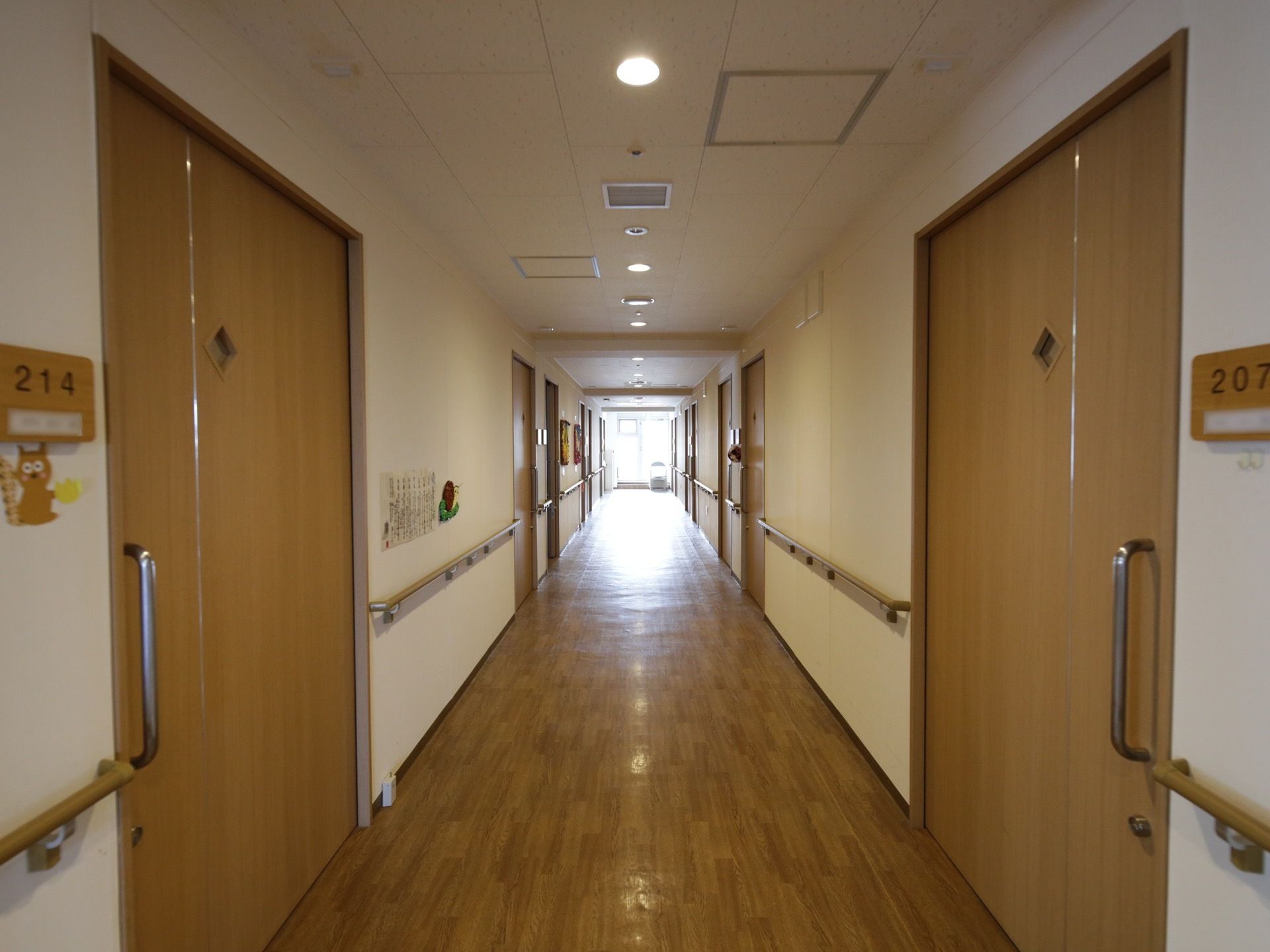直線に伸びた通路の両側に居室がある。奥の窓からは光が良く差し込んでいる。壁には部屋ナンバーが分かり易く表示され、手すりも付いている。