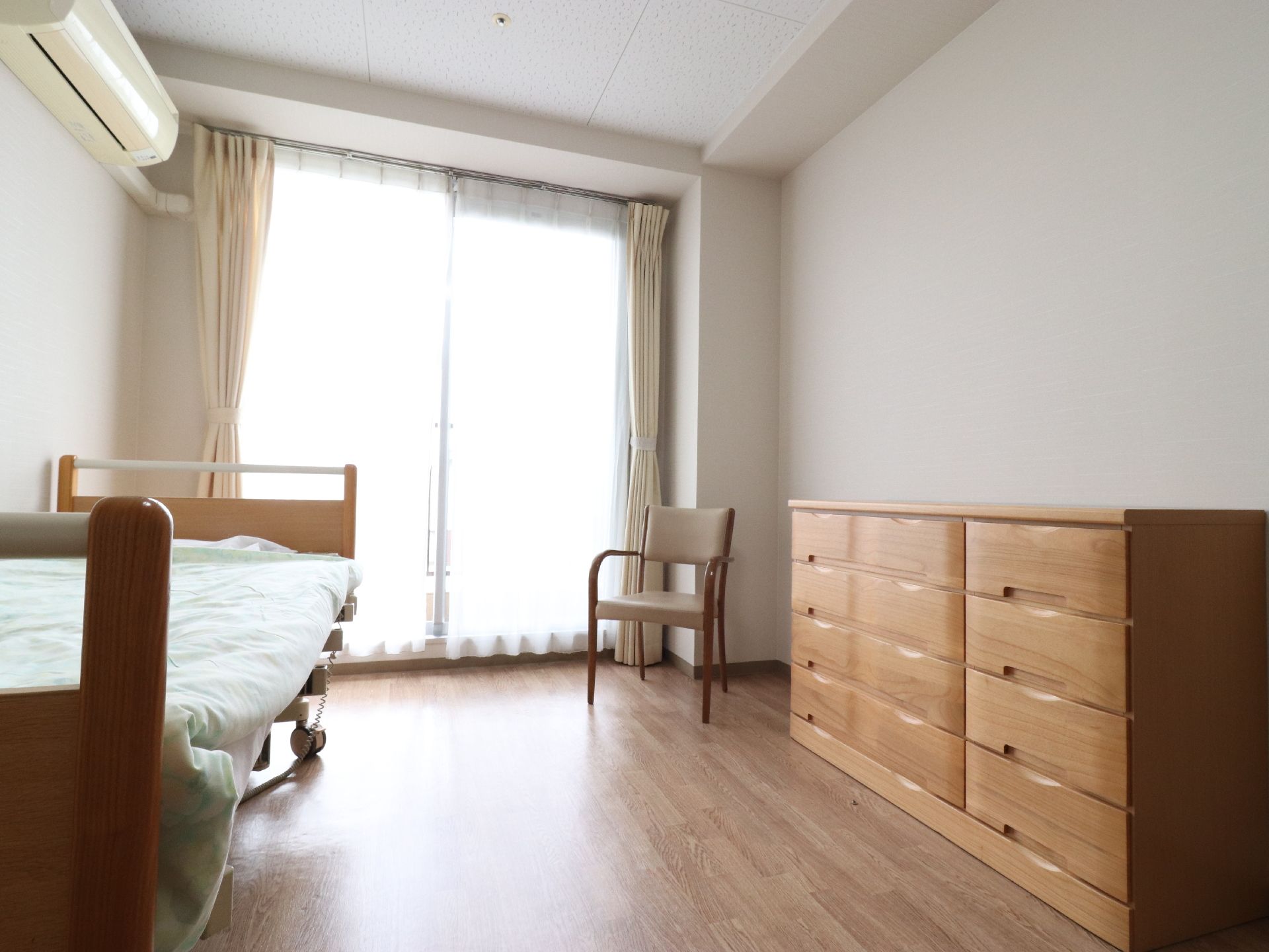 大きな窓の備えられた居室。自然光がふんだんに差し込む明るい構造になっている。収納タンスが設置されている。