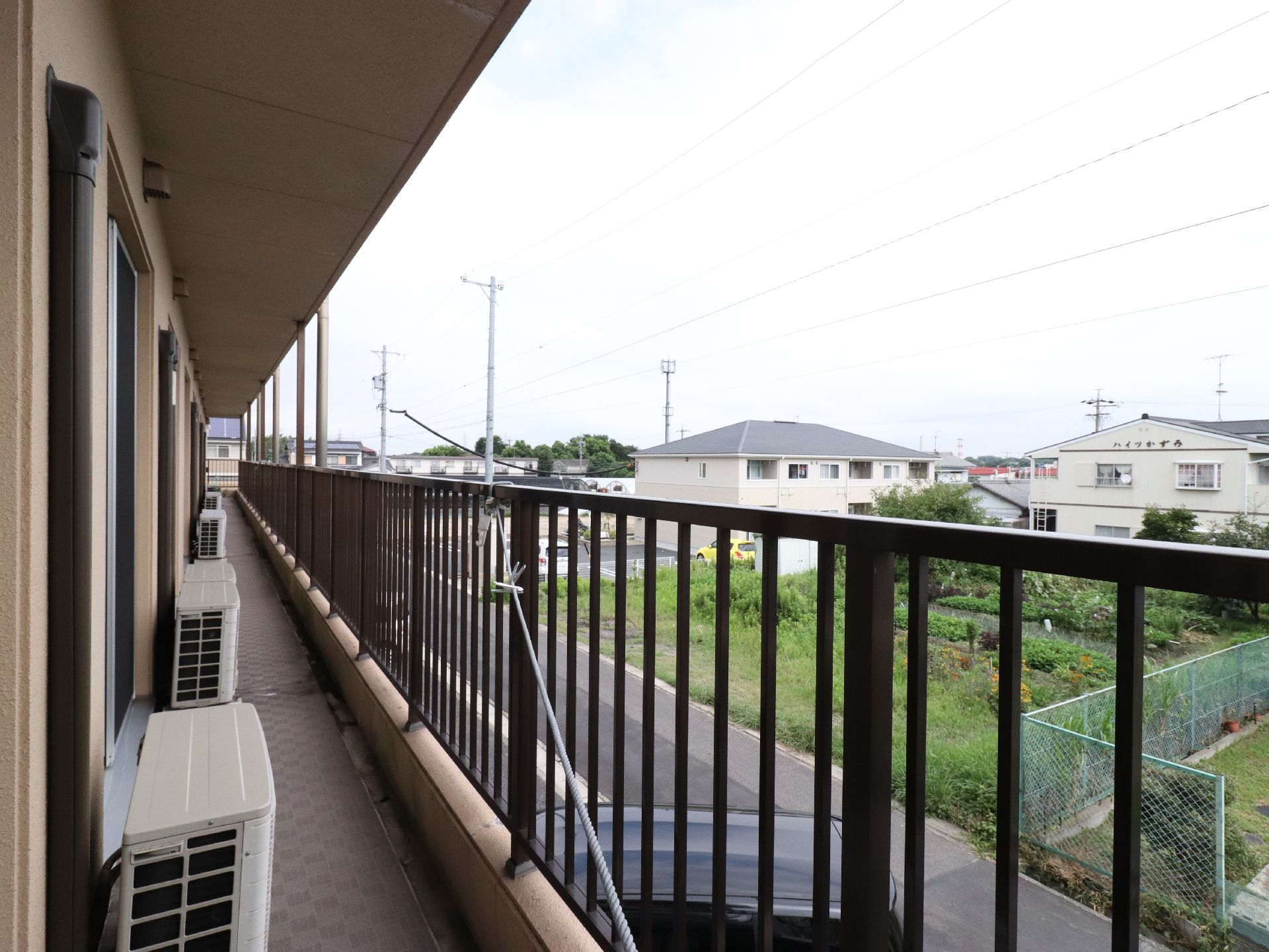 2階のベランダから臨む、近所の景色。背の低い建物と緑が多い田園風景が広がる。頭上にはひさしが張り出し、雨を防いでくれる。