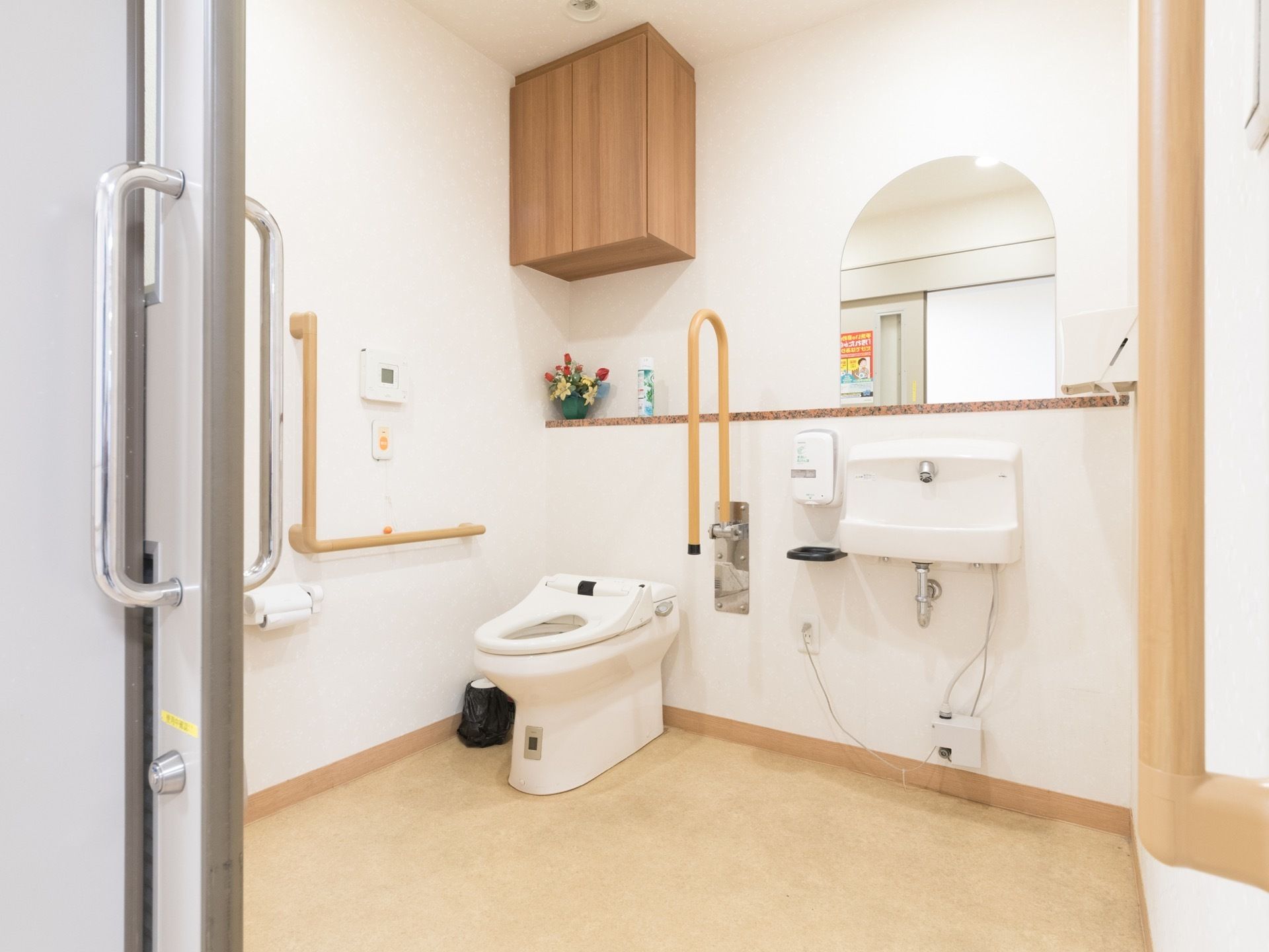 明るく広々としたトイレには洋式トイレと鏡の付いた手洗いが設置されている。周囲の壁には様々な手すりが取り付けられている。