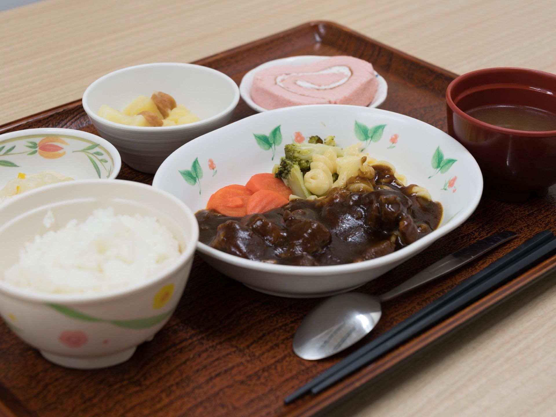 お盆の上に、食事が乗せられて提供される。白いご飯、ビーフシチュー、お味噌汁、漬物、サラダ、ロールケーキが乗っている。