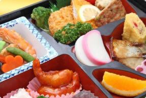 煮物や揚げ物、カットオレンジなどが詰まった弁当