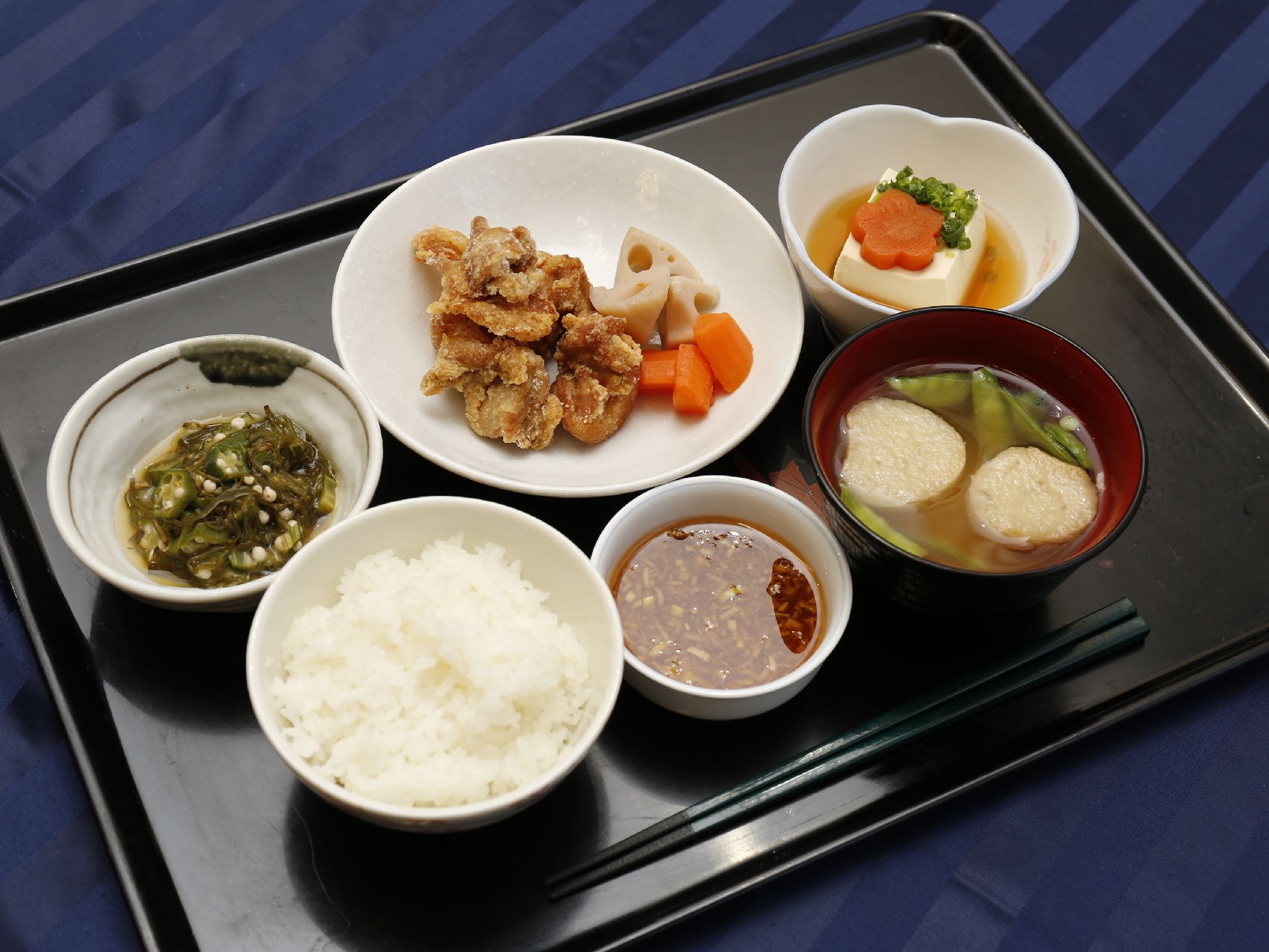 施設で提供される食事の例である。メイン料理の唐揚げと小鉢が2つ、ご飯とみそ汁がある。ほとんどの料理に野菜が入っている。