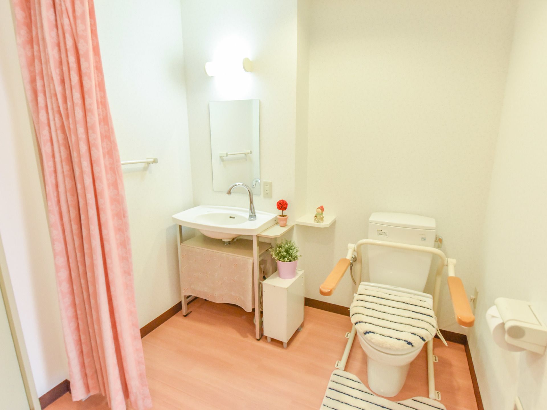 洋式のトイレには可動式の肘掛けが付いており、肘を置く部分は木製。隣にはシンプルな手洗い器が備え付けられている。