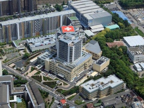 高層マンションに囲まれた中に、同じくらい高い病院が建っている。病院の敷地の一部には樹木が植えられ遊歩道が整備されている。
