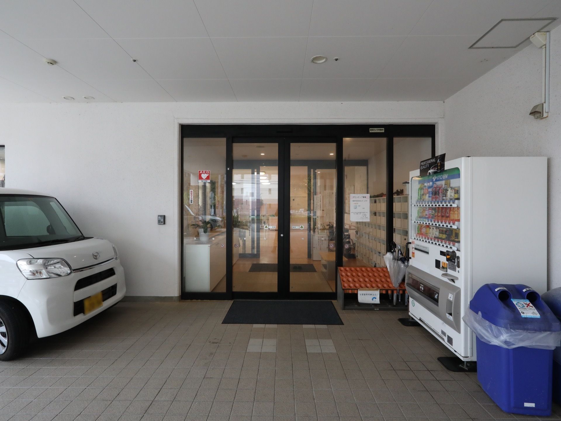 車寄せのできるピロティ付きの玄関。扉は自動ドアで見通しが良くなっている。壁際には自動販売機が設置されている。