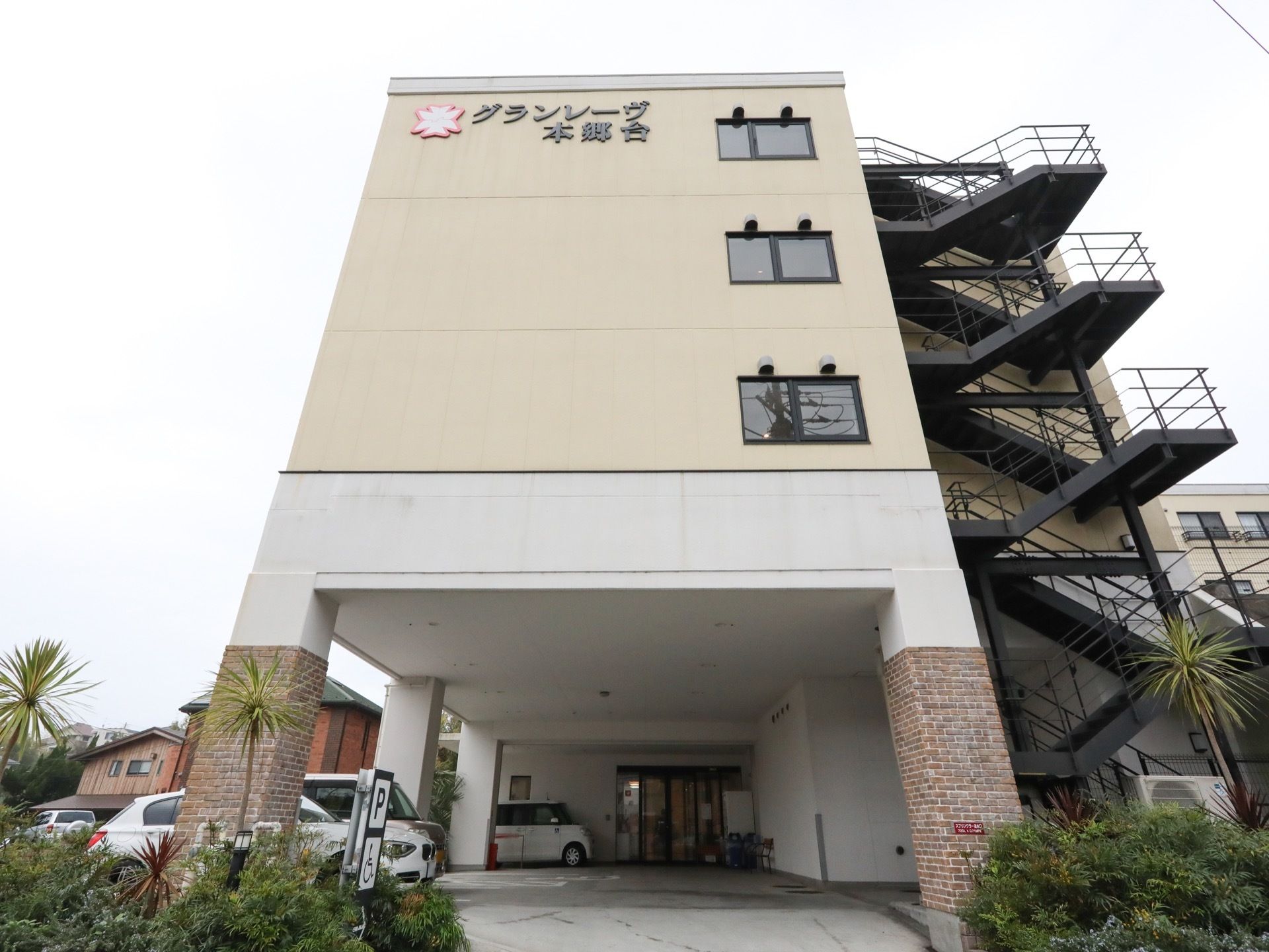 白を基調とした４階建ての住宅が建っている。１階はピロティになっており、奥に自動ドアの付いた玄関が見える。