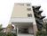 白を基調とした４階建ての住宅が建っている。１階はピロティになっており、奥に自動ドアの付いた玄関が見える。