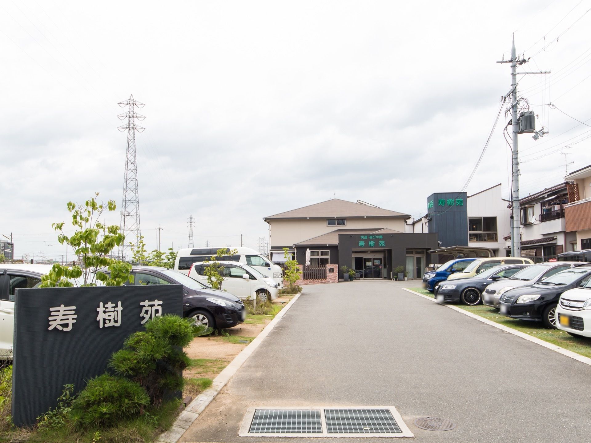 敷地の入り口に、施設名が表示された大きな看板が立てられている。敷地内には駐車スペースが多数備えられている。